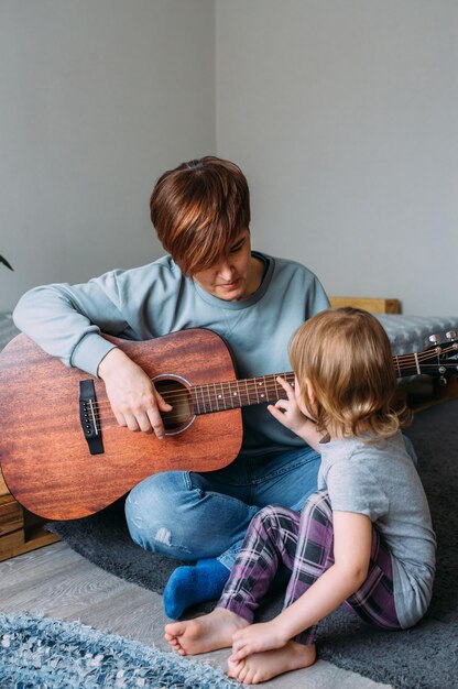 La bambina suona la chitarra con sua madre sul pavimento di casa