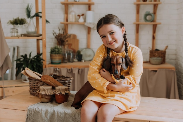 La bambina sveglia a casa in cucina cuoce i biscotti con il suo cane bassotto