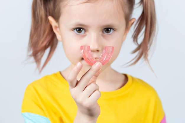 La bambina sveglia con i capelli biondi tiene in mano un trainer miofunzionale dentale rosa