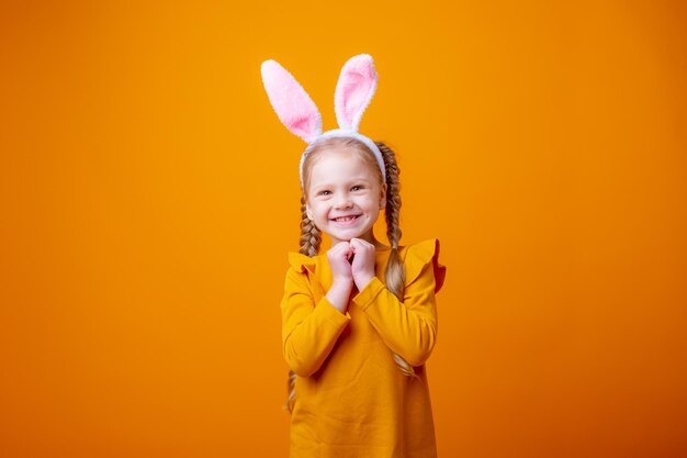 La bambina sveglia con l'orecchio del coniglietto di Pasqua su fondo giallo mostra il sogno di gioia di emozioni differenti