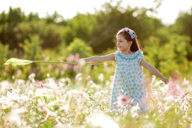 La bambina sveglia con una corona sulla sua testa cammina in un campo e prende la rete delle farfalle