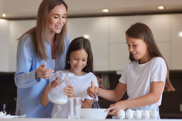 La bambina sveglia e la sua bella mamma in grembiule giocano e ridono mentre impastano la pasta in cucina