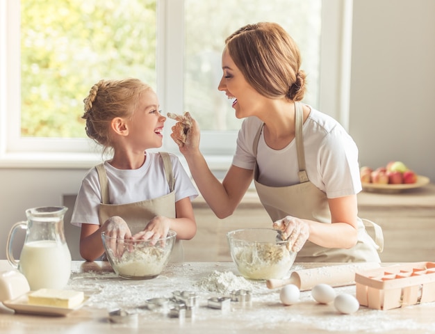 La bambina sveglia e la sua bella mamma in grembiuli stanno giocando