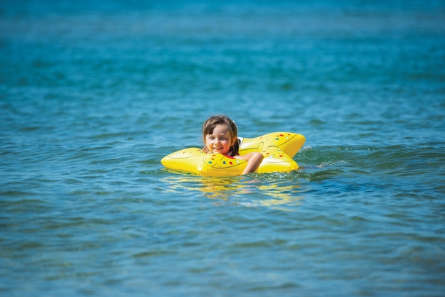 La bambina sveglia in costume da bagno con una stella marina gonfiabile nuota nel mare. Umore positivo, buone feste e divertimento.