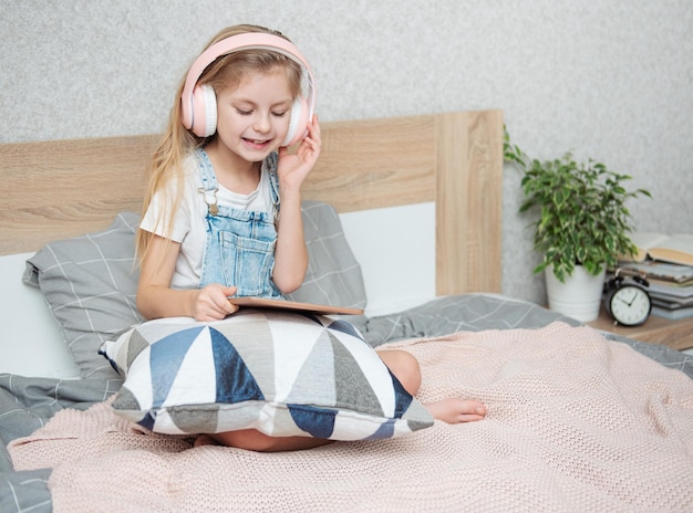 La bambina sveglia in cuffia sta usando un tablet a casa