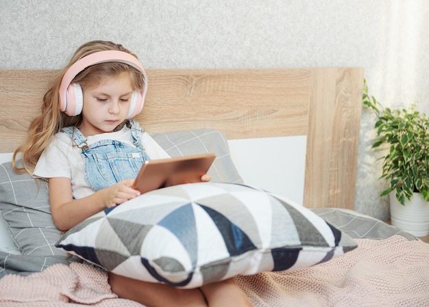 La bambina sveglia in cuffia sta usando un tablet a casa