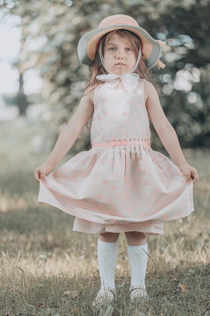 La bambina sveglia in un vestito rosa con un cappello sta nel parco di estate. Foto di alta qualità