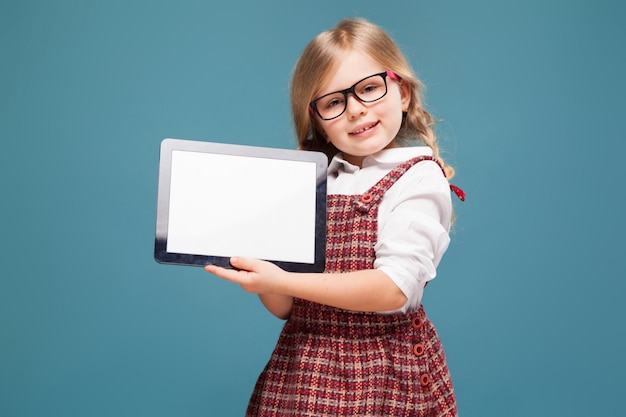 La bambina sveglia in vestito rosso, camicia bianca e vetri tiene la compressa vuota