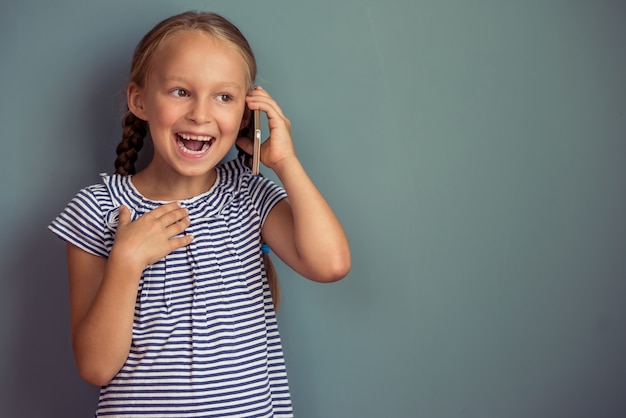 La bambina sveglia in vestito sta parlando sul telefono cellulare