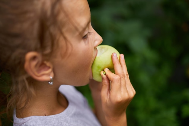 La bambina sveglia mangia la mela verde nel bambino felice all'aperto del giardino di casa