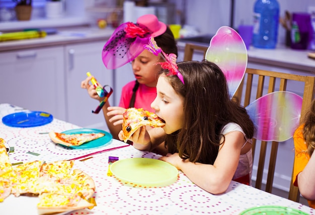La bambina sveglia mangia la pizza alla festa Bella ragazza in costume da farfalla Festa di compleanno con gli amici