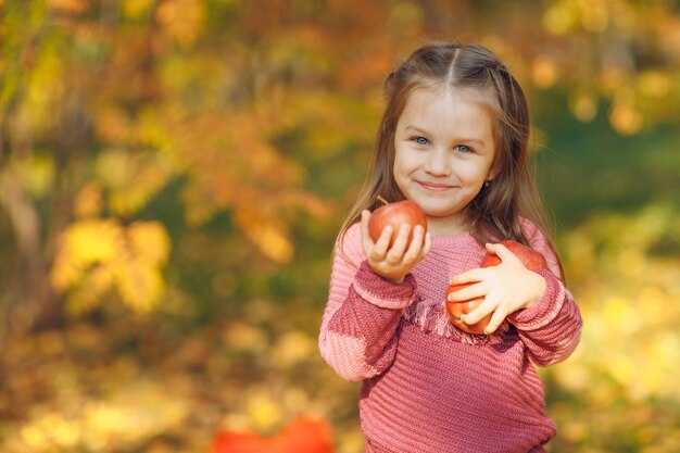 La bambina sveglia nella sosta di autunno tiene le mele rosse nelle mani.