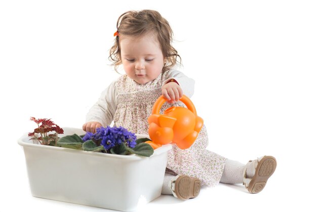 La bambina sveglia versa i fiori in una pentola su una priorità bassa bianca