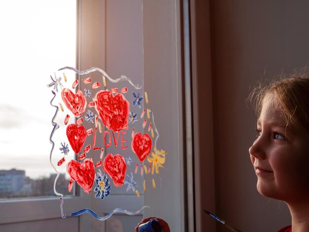 La bambina tiene in mano il pennello disegnando un cuore rosso sul vetro della finestra San Valentino amore datazione tempo libero in quarantena