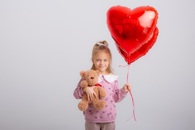 la bambina tiene palloncini a forma di cuore e orsacchiotto su sfondo bianco