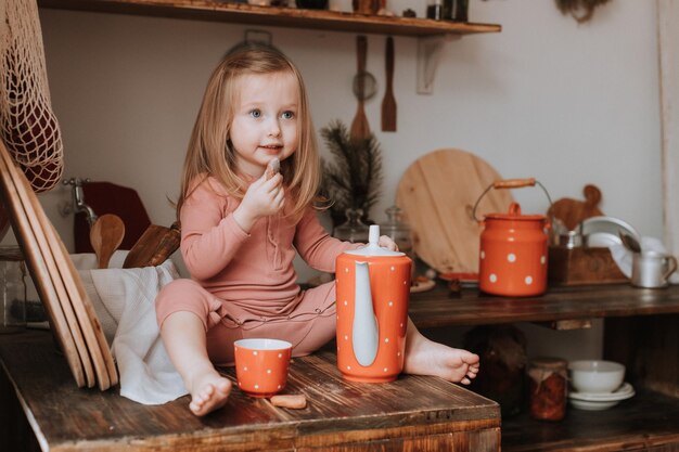 la bambina versa il tè in una tazza da una teiera piatti in ceramica rossa nella cucina in legno di piselli bianchi