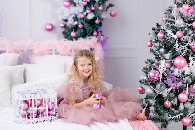 La bambina veste l'albero di Natale con un bellissimo vestito rosa