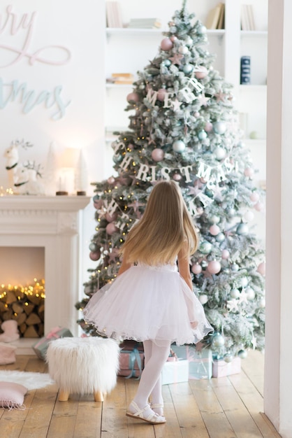 la bambina, vestita con un bellissimo abito bianco alla moda, posa vicino all'albero di Natale.