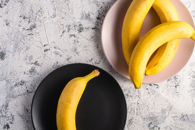La banana fruttifica in piastre rosa e nere su superficie strutturata bianca, spazio della copia di vista superiore