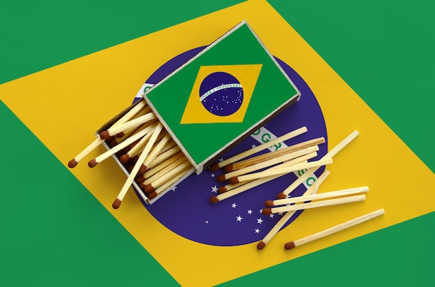 La bandiera del Brasile è mostrata su una scatola di fiammiferi aperta, da cui cadono diverse partite e si trova su una grande bandiera