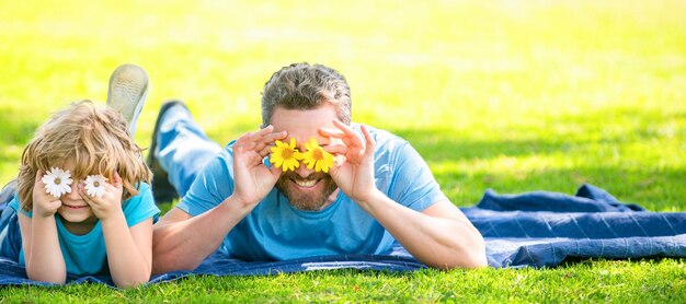 La bandiera del padre felice con il bambino si rilassa insieme sull'erba verde del parco divertendosi con i fiori famiglia felice