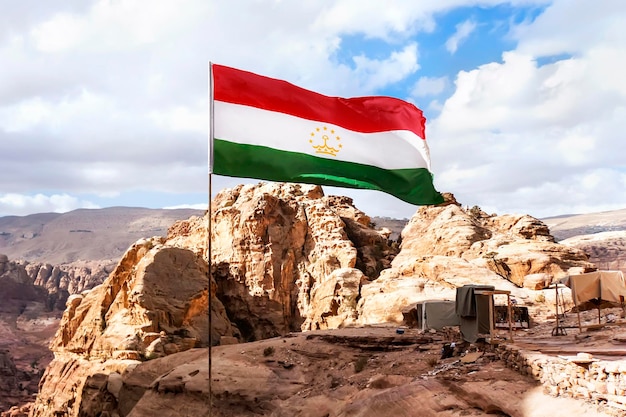 La bandiera del Tagikistan sta volando nel vento contro un cielo nuvoloso in montagna