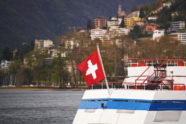 La bandiera della Svizzera sventola su una barca turistica sul Lago di Lugano Una bandiera rossa con una croce bianca sopra