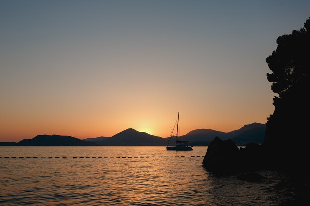 La barca a vela salpa da dietro le rocce al tramonto