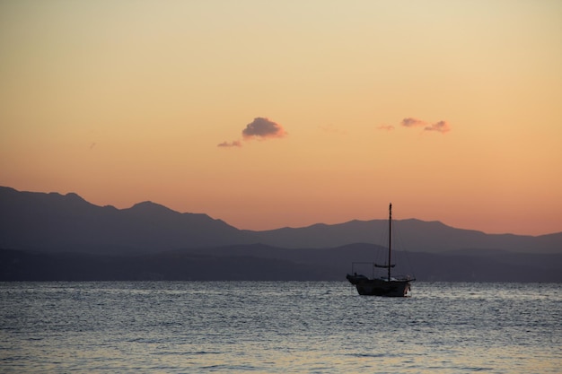 La barca naviga in riva al mare all'alba sullo sfondo della montagna.