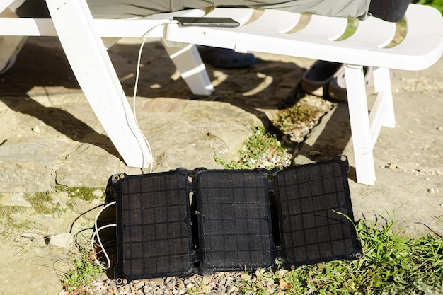 La batteria solare si trova a terra vicino alla sedia di plastica su cui viene caricato il telefono cellulare Concetto di fonte di energia alternativa