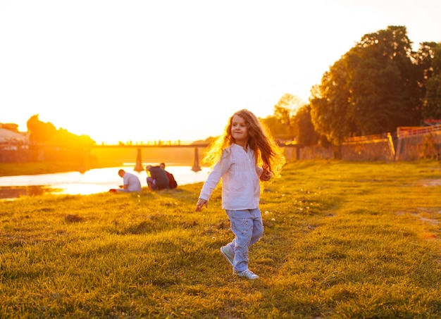 La bella bambina con i capelli lussuosi sta ballando vicino al fiume durante il tramonto