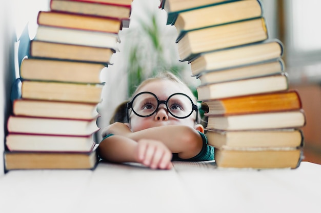 La bella bambina divertente con gli occhiali rotondi guarda in alto molti libri che si preparano per la scuola Concetto di istruzione elementare