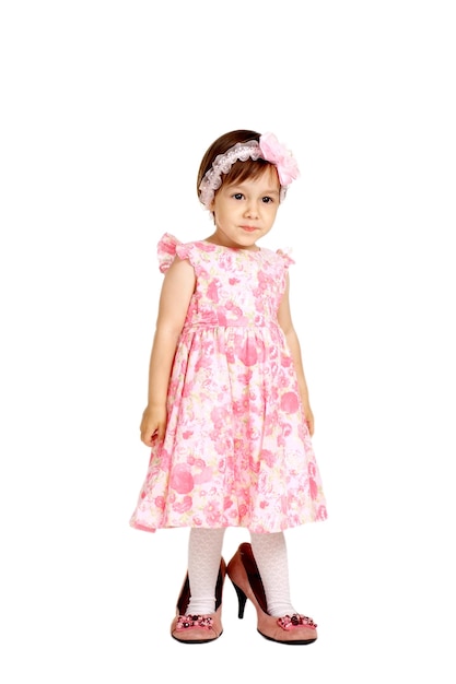 La bella bambina in un vestito rosa e nelle grandi scarpe sta su un fondo bianco