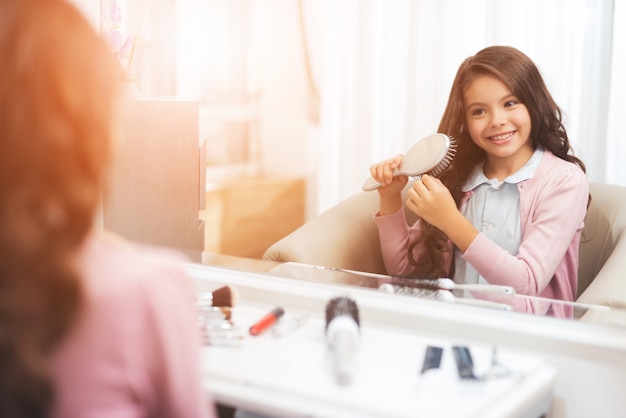 La bella bambina sta pettinando i suoi capelli nel salone di bellezza.