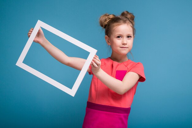 La bella bambina sveglia in vestito rosa tiene la cornice