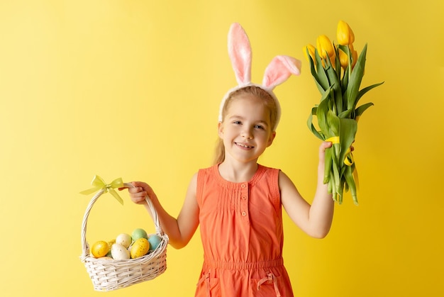 La bella bambina sveglia nelle orecchie del coniglietto di Pasqua tiene un cestino con le uova e il mazzo della molla