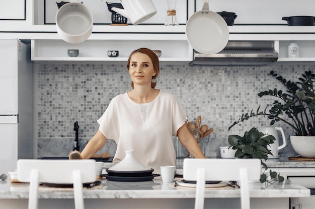 La bella casalinga bionda sta per preparare il cibo per la sua famiglia dalla cucina a luce bianca. Concetto di cura