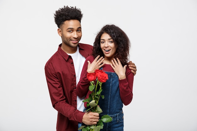 La bella coppia elegante sta abbracciando e sorridendo, su fondo grigio. La ragazza sta tenendo le rose