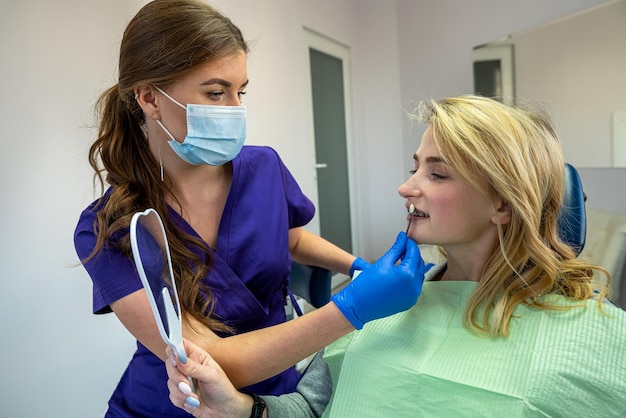 La bella dentista femminile in abiti speciali seleziona il colore naturale dei denti per lo sbiancamento di un paziente Concetto di sbiancamento dei denti