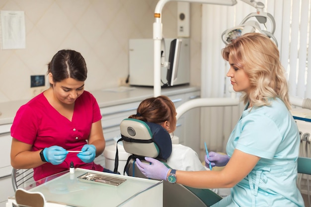 La bella dentista femminile tratta un paziente sul posto di lavoro in clinica odontoiatrica