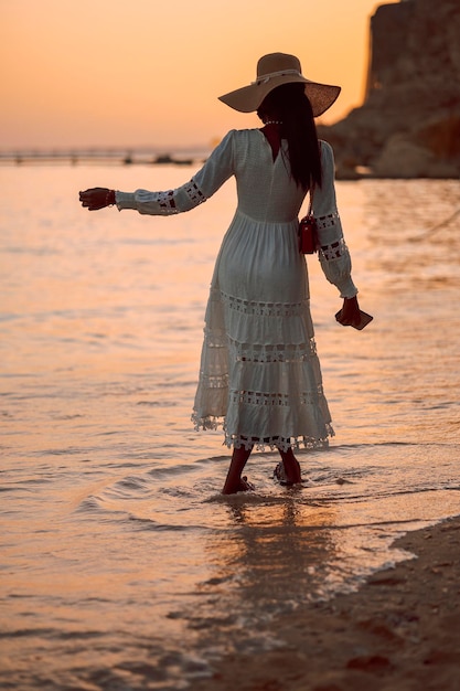 La bella donna africana in cappello del sole cammina sulla spiaggia