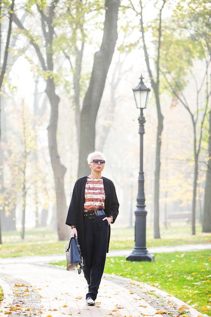 La bella donna alla moda bionda cammina nella sosta di autunno