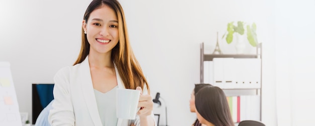 La bella donna asiatica autorizza la donna che tiene una tazza di caffè e un amico che lavora nella sala riunioni in ufficio Avvio di una donna d'affari con fiducioso e allegro