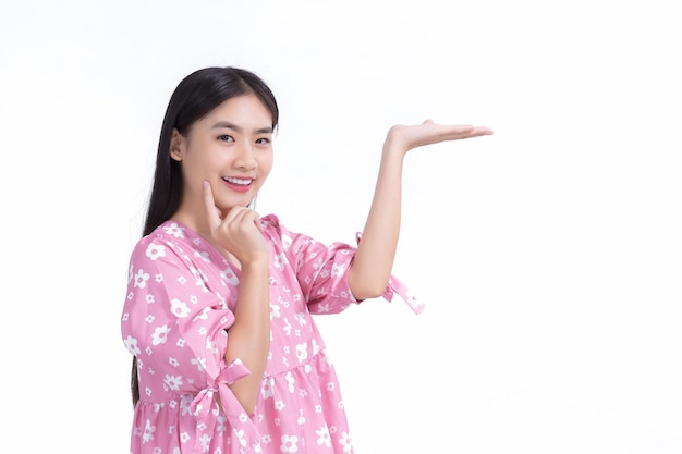 La bella donna asiatica con i capelli lunghi neri in camicia rosa mostra presenta qualcosa di sfondo bianco