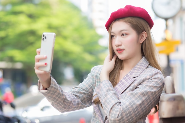 La bella donna asiatica in capelli bronze prende la foto del selfie dallo smartphone sulla via come fondo.