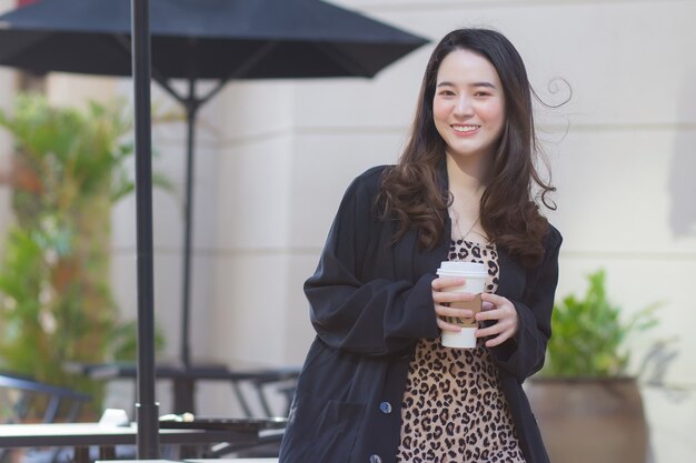 La bella donna asiatica in un vestito blu scuro sta sorridendo felice davanti alla caffetteria