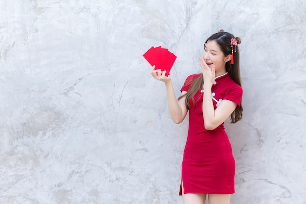 La bella donna asiatica in vestito rosso sta e tiene una busta rossa con un'espressione eccitata