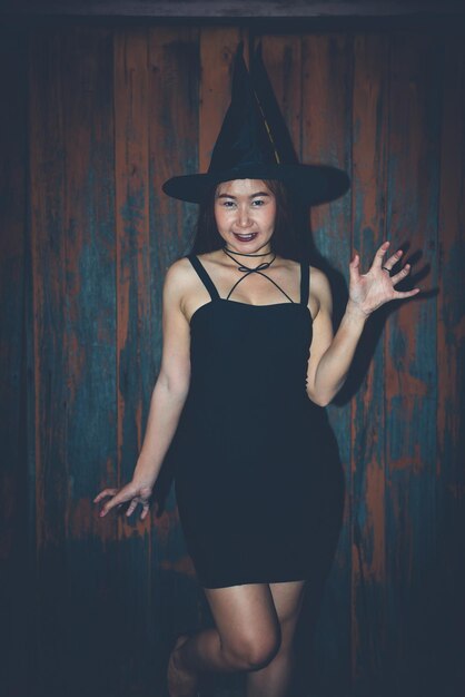 La bella donna asiatica indossa un vestito nero con il cappello della strega alla ferrovia sul concetto della Tailandia del tramonto di Halloween