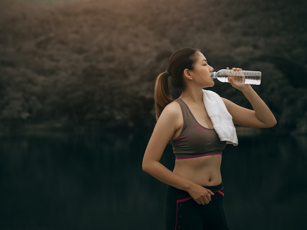 La bella donna asiatica si esercita fuori e beve l'acqua