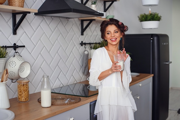 La bella donna beve il latte a colazione, nell'elegante cucina accogliente. Concetto di dieta e alimentazione sana.